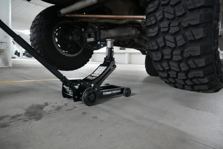 Titan Terrain 1.7 tonne low profile slim floor jack lifting a 4WD rear differential with a V-type adapter in a concrete garage.